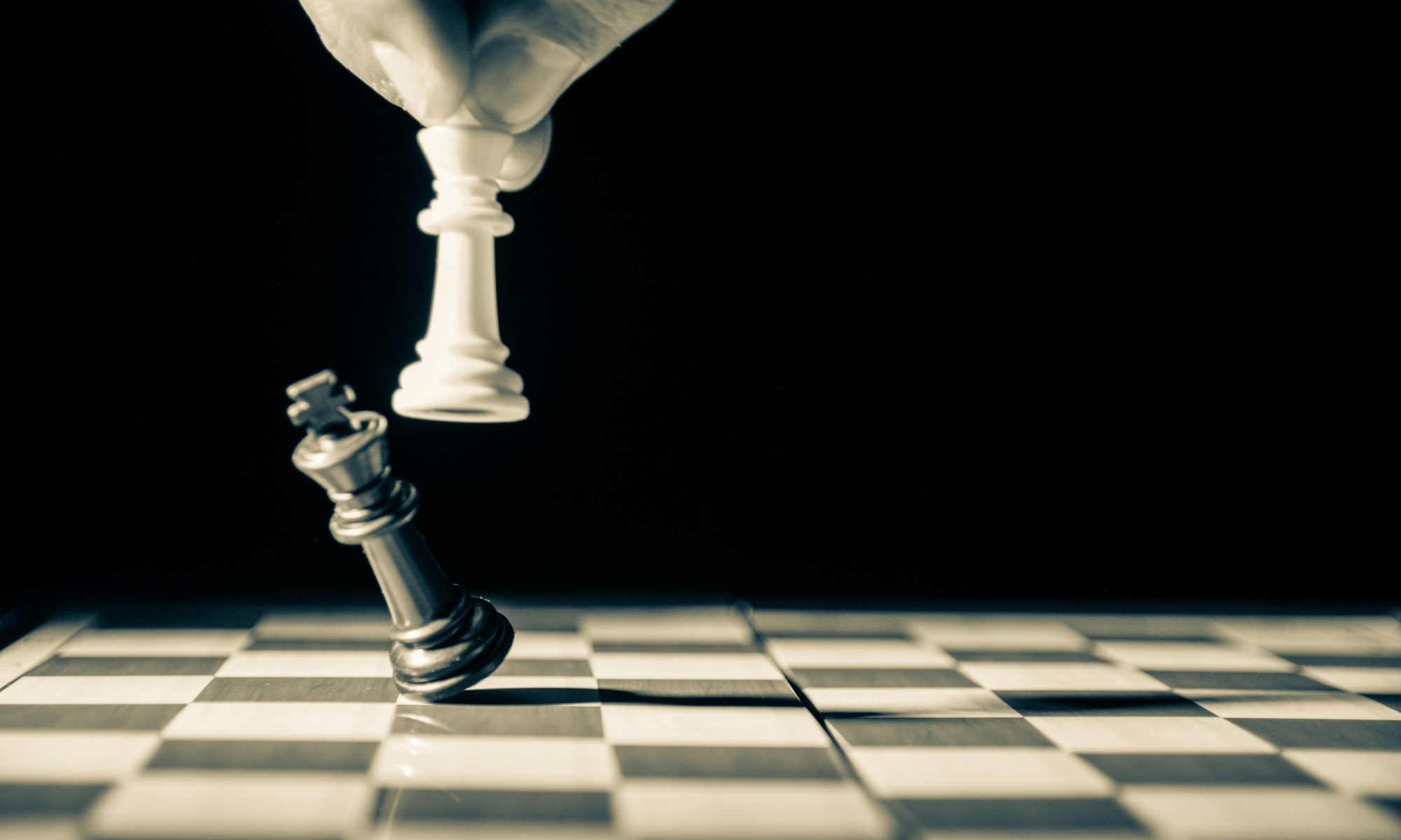 Close up of white king taking down black king. Hand and fingers and chess board with vintage look. Photo by GR Stocks on Unsplash